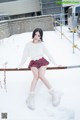 A woman in a white sweater and plaid skirt posing in the snow.