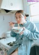 A woman holding a bowl of noodles in a kitchen.