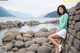 A woman leaning against a stone wall by the water.