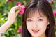 A woman holding a pink flower in front of her face.