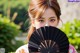 A woman holding a black fan in front of her face.