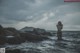 A naked woman standing in the ocean with her hands on her head.