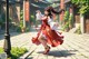 A woman in a red and white dress dancing in a courtyard.