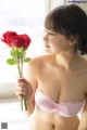 A woman in a pink bra holding a red rose.